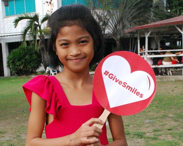 Girl holds sign that says Give Smiles